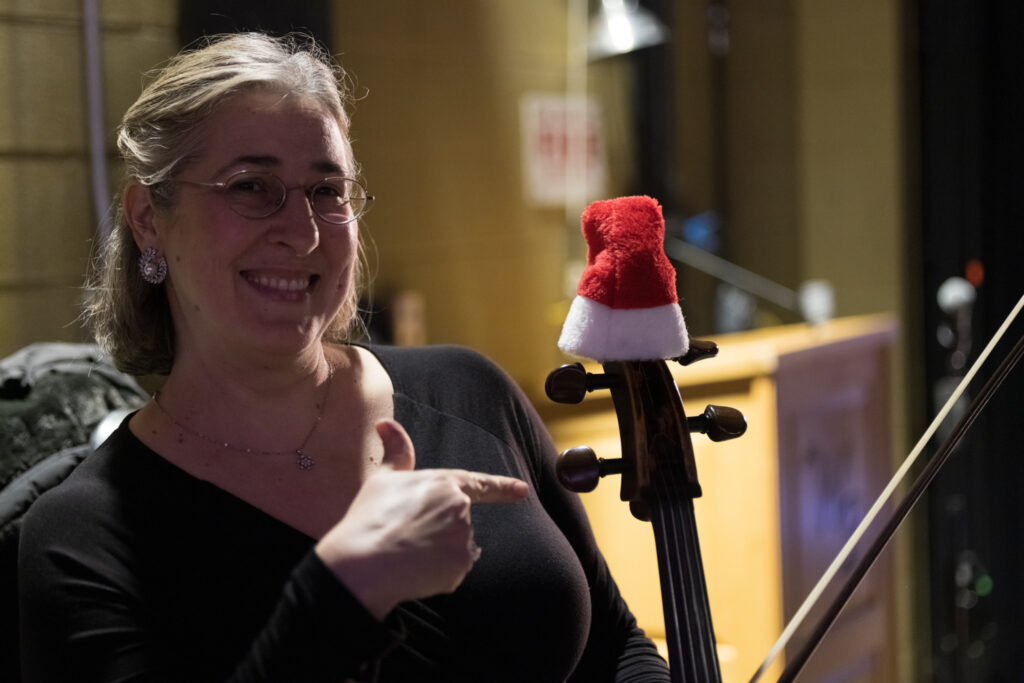 A musician points to her instrument that has a small Santa Claus hat.